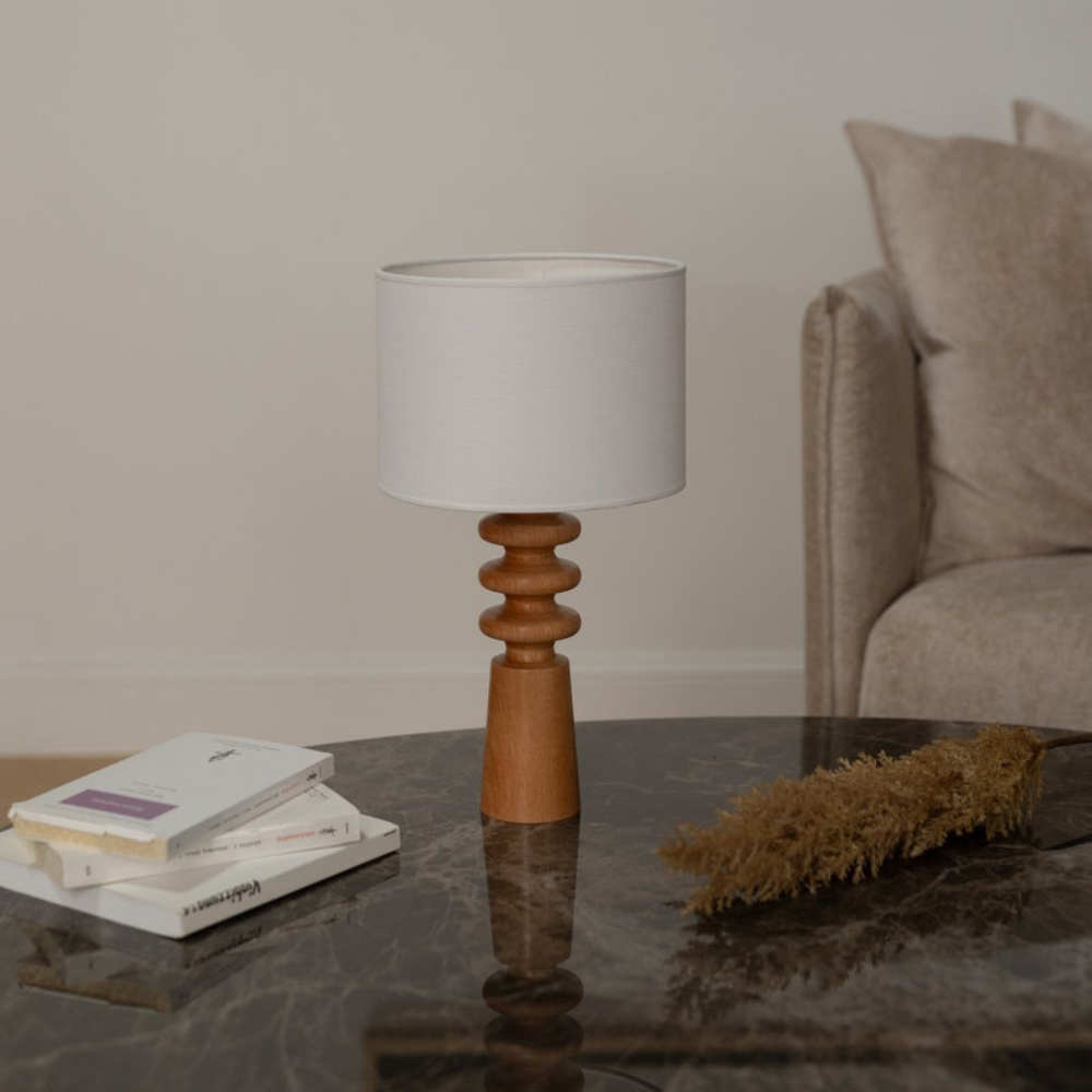 Verschönern Sie Ihren Wohnraum mit dieser eleganten Tischleuchte aus Holz mit einem skulpturalen Sockel und einem klassischen Lampenschirm aus Stoff. Die warmen Holztöne in Kombination mit dem minimalistischen Design machen sie zu einer vielseitigen Ergänzung für jedes Interieur, von modern bis rustikal. Diese Lampe eignet sich perfekt für Nachttische, Wohnzimmer oder Heimbüros und sorgt für ein sanftes Umgebungslicht, das eine gemütliche Atmosphäre schafft. Der handgefertigte Holzsockel verleiht ihr einen