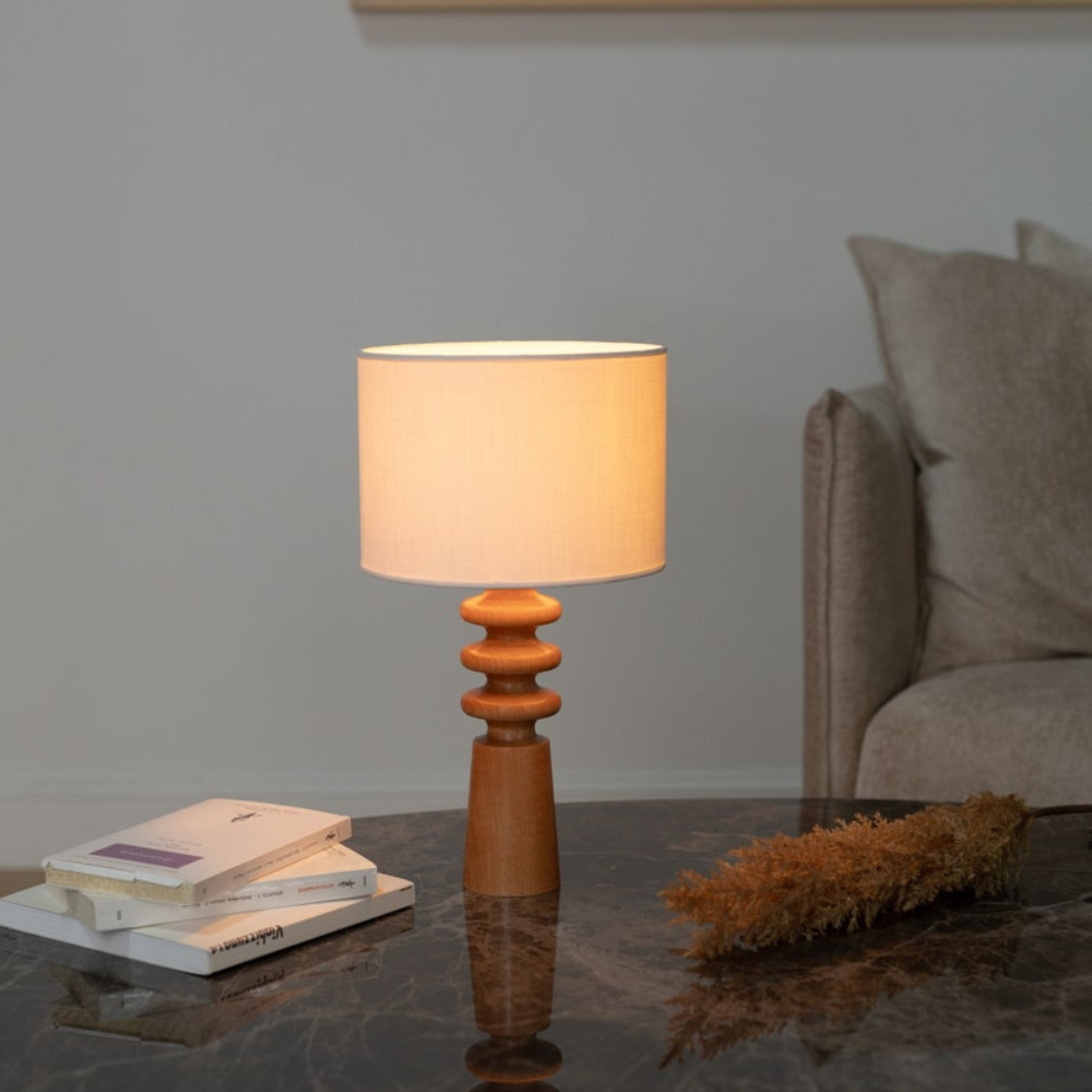 Verschönern Sie Ihren Wohnraum mit dieser eleganten Tischleuchte aus Holz mit einem skulpturalen Sockel und einem klassischen Lampenschirm aus Stoff. Die warmen Holztöne in Kombination mit dem minimalistischen Design machen sie zu einer vielseitigen Ergänzung für jedes Interieur, von modern bis rustikal. Diese Lampe eignet sich perfekt für Nachttische, Wohnzimmer oder Heimbüros und sorgt für ein sanftes Umgebungslicht, das eine gemütliche Atmosphäre schafft. Der handgefertigte Holzsockel verleiht ihr einen